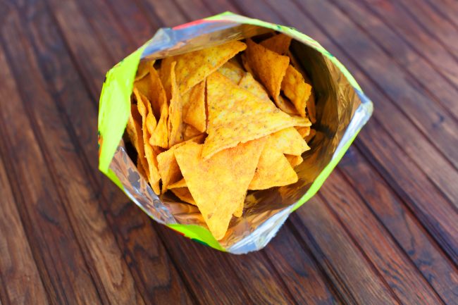 Opened pack of delicious nachos corn chips on a rustic wooden background. Horizontal view from above shrinking snack sizes