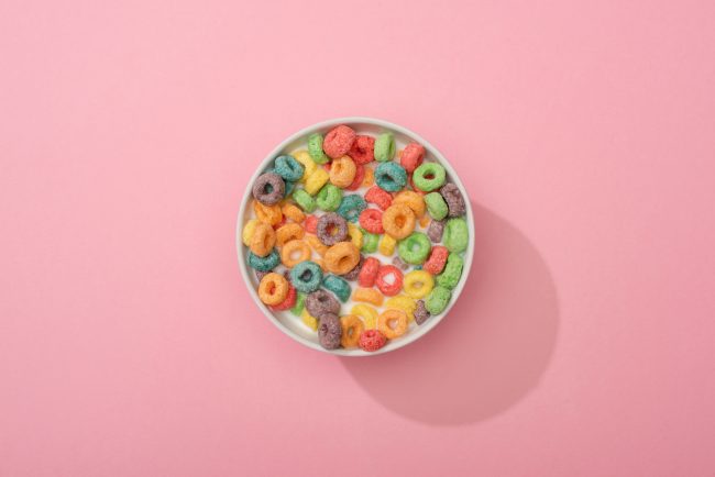 top view of bright colorful breakfast cereal in bowl on pink background grocery items