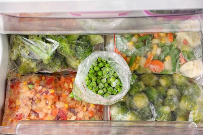 Plastic bags with frozen green peas and different vegetables in refrigerator frozen vegetables