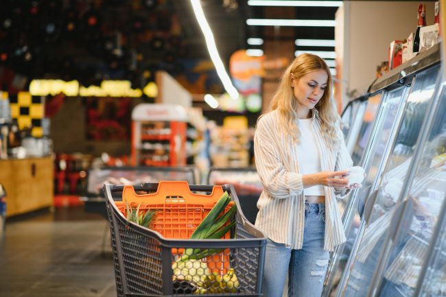 Young woman looking at product at grocery store. Costumer buying food at the market grocery prices