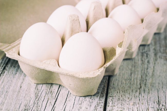 Cardboard egg rack with eggs on white wooden table budget foods that aren’t budget-friendly