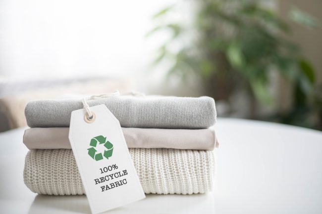 A neat stack of knitted clothing with a 100 percent recycle fabric label. White background. eco-friendly labels