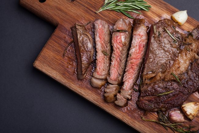 Grilled rib-eye steak of marble beef closeup with spices on a wooden Board. Juicy steak medium sliced and ready to eat. With copy space steak cuts