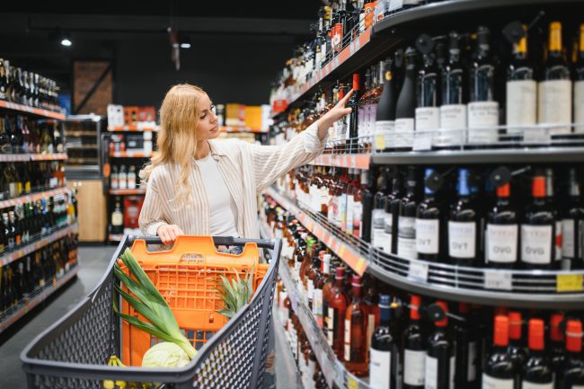 girl chooses wine in supermarket. girl reads labels on bottles of wine in supermarket grocery shopping on weekends