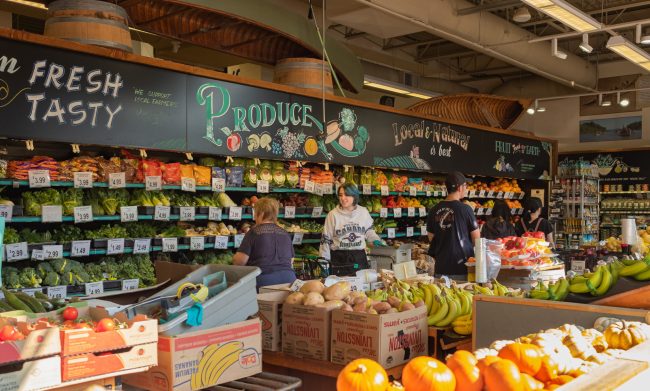 People shopping in the market. Buyer Shopping Groceries In store. Woman employee restocking the shelves in grocery store produce aisle at the front