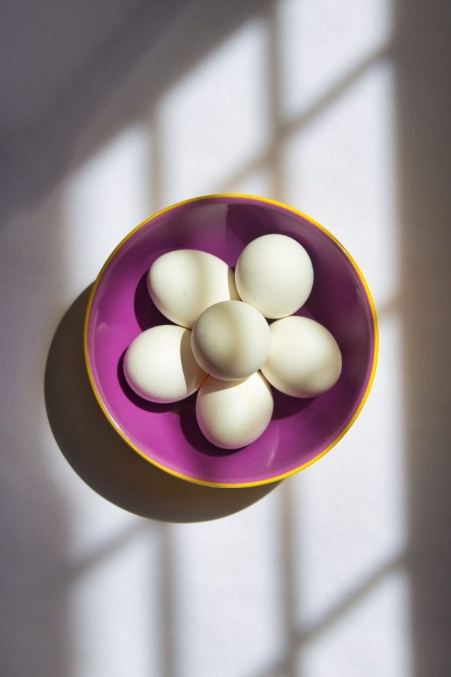White eggs arranged in a purple bowl on a light surface. 9 Grocery Items That Were Cheaper at Walmart Than Kroger and Amazon