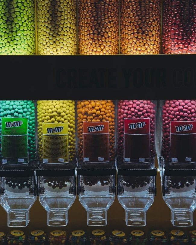 Rows of clear plastic candy dispensers filled with M&Ms. The Grocery Departments Seeing the Biggest Price Changes This Year