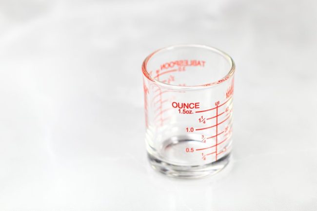 A small glass measuring cup with red markings showing fluid ounce increments. The 'Per-Ounce Rule' That Could Save You Hundreds on Groceries This Year
