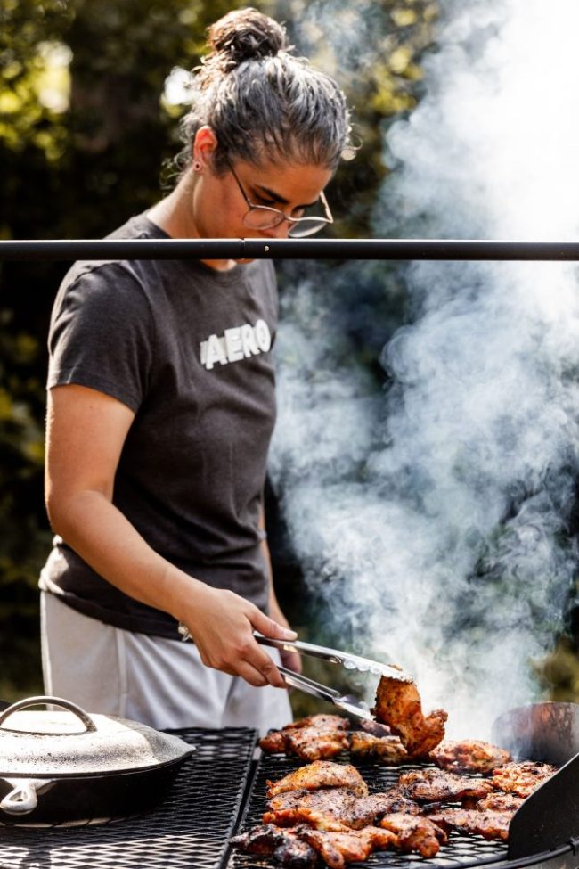 A person using tongs to grill meat over an open flame outdoors. Buying Meat for the Week? These 6 Price-Per-Pound Traps Can Wreck Your Budget