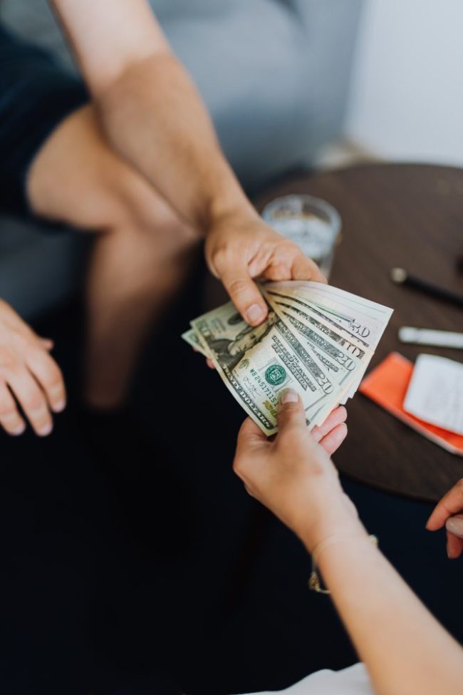 One person handing a stack of US dollar bills to another person. Digital-Only Grocery Deals Can Leave Some Shoppers Paying More