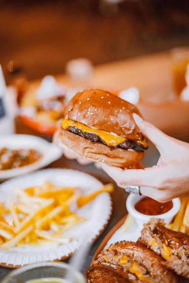 A person holding a freshly made cheeseburger with melted cheese on a sesame seed bun. National Cheeseburger Day Is Friday — Here Are the Best $1, Free and Discounted Burger Deals