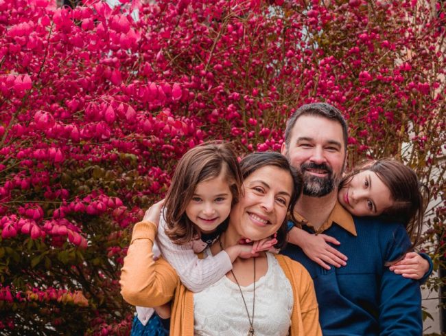 A smiling family of four posing outdoors in front of a vibrant bush with bright pink leaves. Fast Food for a Family of 4: What $40 Actually Buys at 6 Major Chains