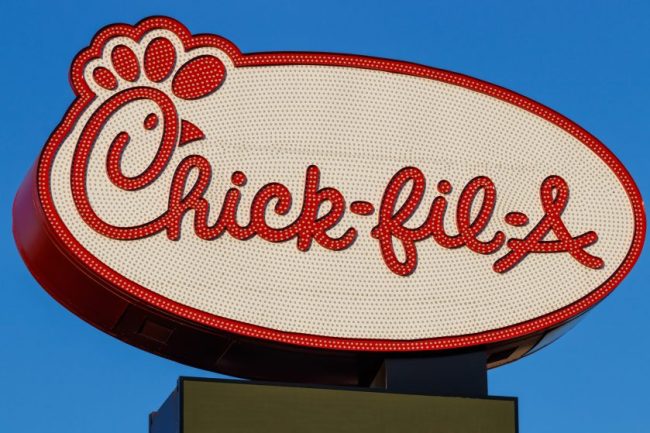 The illuminated Chick-fil-A logo sign featuring the distinctive red cow and lettering against a blue sky. 9 Chick-fil-A Ordering Hacks Employees and Regulars Say Are Worth Trying