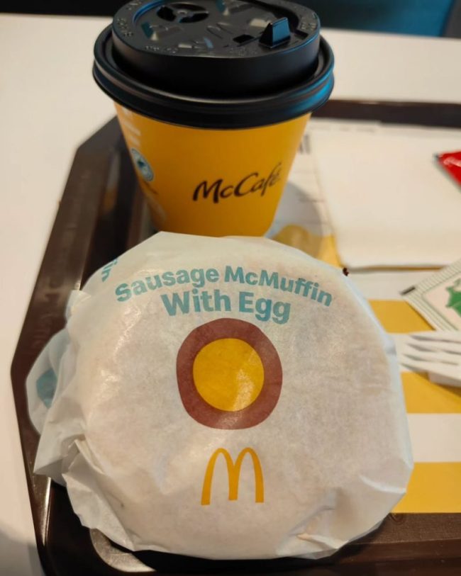 A wrapped Sausage McMuffin with Egg sits next to a yellow McCafé coffee cup. These 7 Fast-Food Deals Are Only Available If You Order Through the App