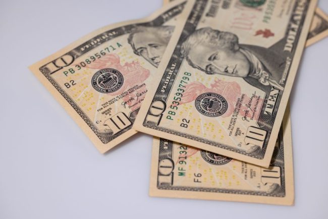 Several ten-dollar bills spread out on a flat surface. The Fast-Food Menu Says $10 — The App Says $6. Why Are Customers Paying Different Prices?