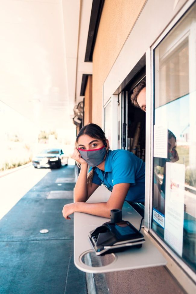 A fast-food worker leaning out of a drive-thru window waiting for customers. 9 Things Drive-Thru Workers Wish Customers Would Stop Doing