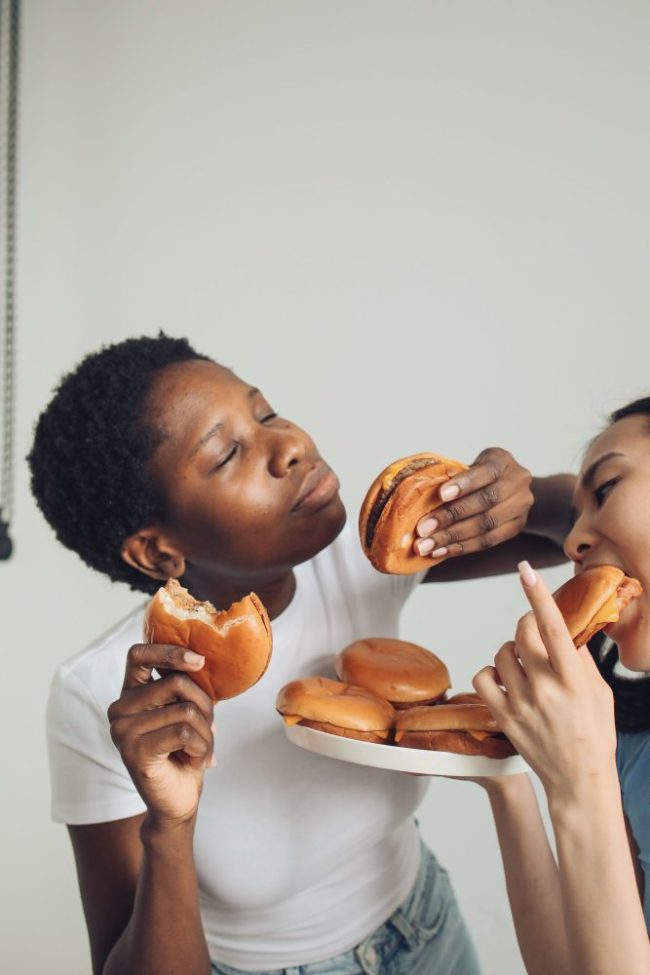 Two people holding and eating small burgers from a plate. Why Your Favorite Fast-Food Order Costs More Than You Remember