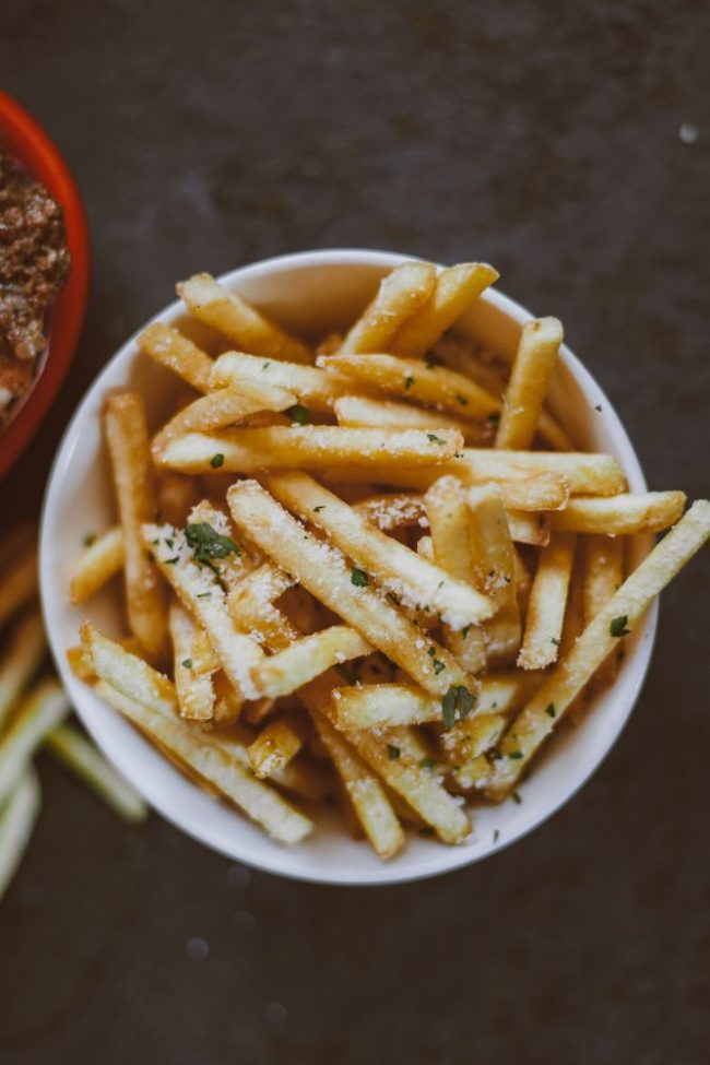 A bowl of seasoned French fries tossed with grated cheese and fresh herbs. 8 Fast-Food Items Employees Say Are Better When You Order Them This Way