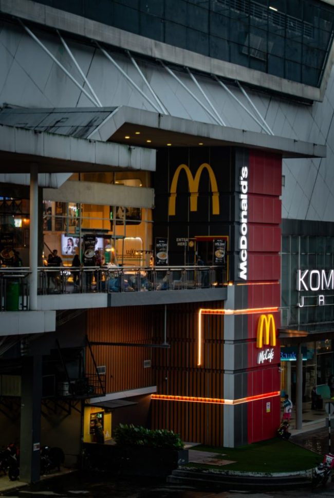 The illuminated storefront sign and golden arches of a multi-level McDonald’s restaurant. McDonald’s Regulars Know These 14 Ordering Tricks — Do You?