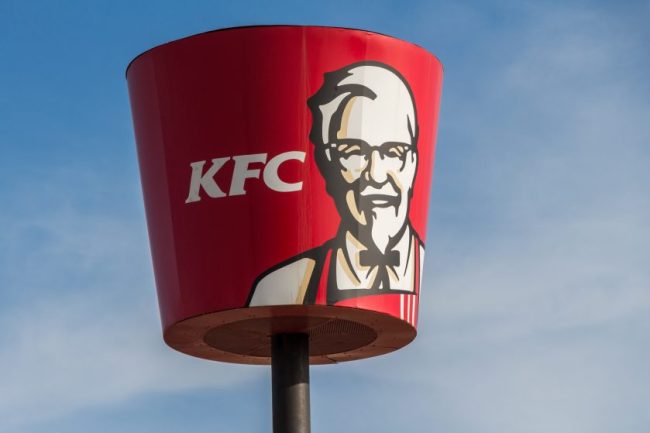 A large red KFC bucket sign featuring the image of Colonel Sanders against a blue sky. Fast Food for 4 People Under $25? We Found Out Which Chains Can Still Do It