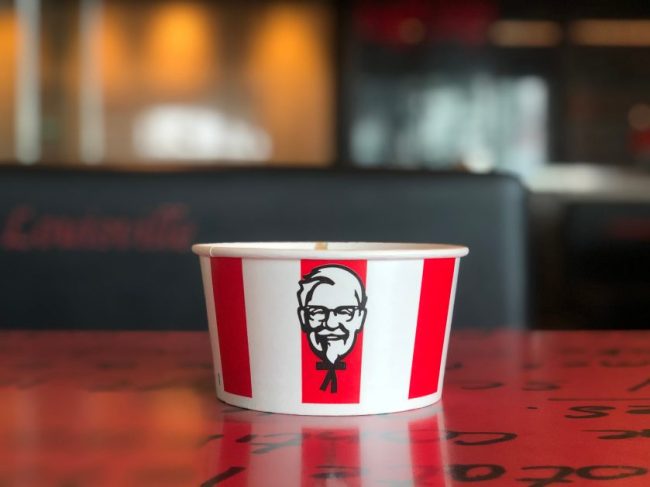 A small white and red KFC paper bucket sitting on a restaurant table. $5 Fast-Food Deals Are Back, But Is Five Bucks Enough for a Real Meal?