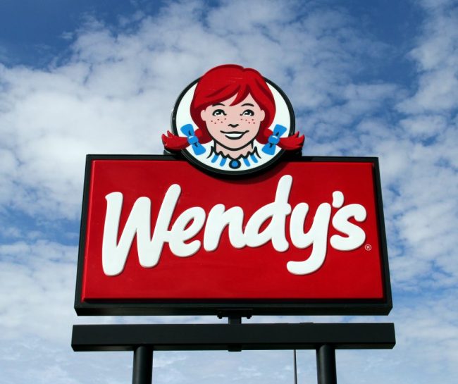 The red-and-white outdoor sign for a Wendy’s restaurant against a blue sky with clouds. 7 Wendy’s App Tricks That Can Make a Cheap Meal Even Cheaper